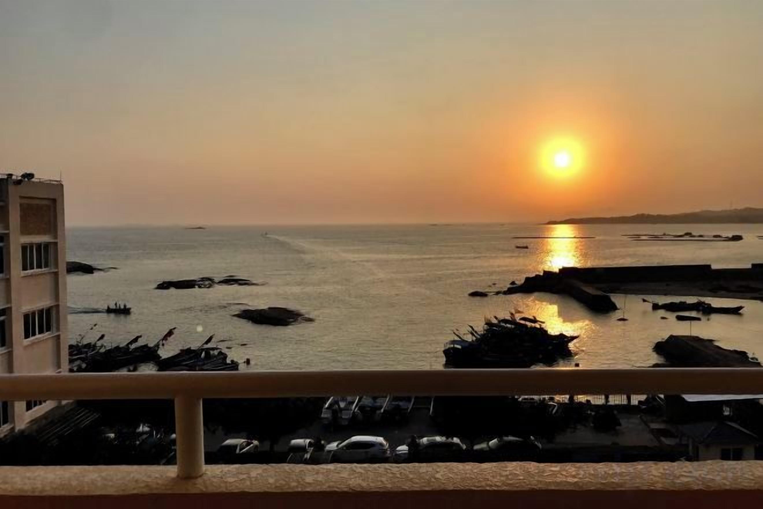 A sunset view from a balcony overlooking a marina with boats and a building in the foreground.