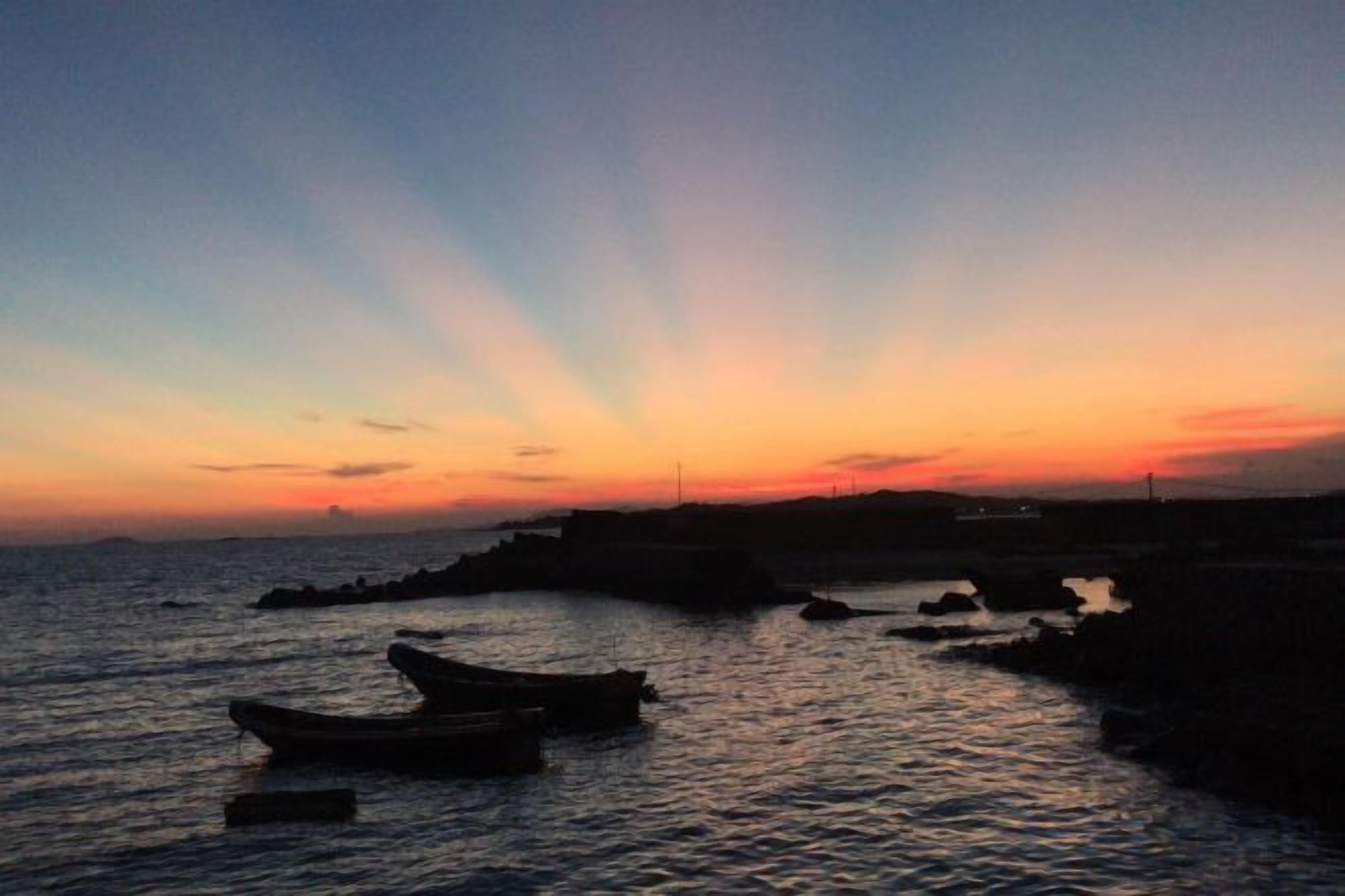 Un atardecer sobre una superficie acuática tranquila con barcos y una costa distante.