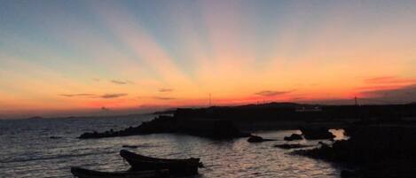 Un atardecer sobre una superficie acuática tranquila con barcos y una costa distante.