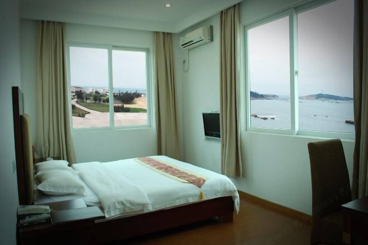 Een hotelkamer met een bed, een televisie, een bureau en uitzicht op zee.