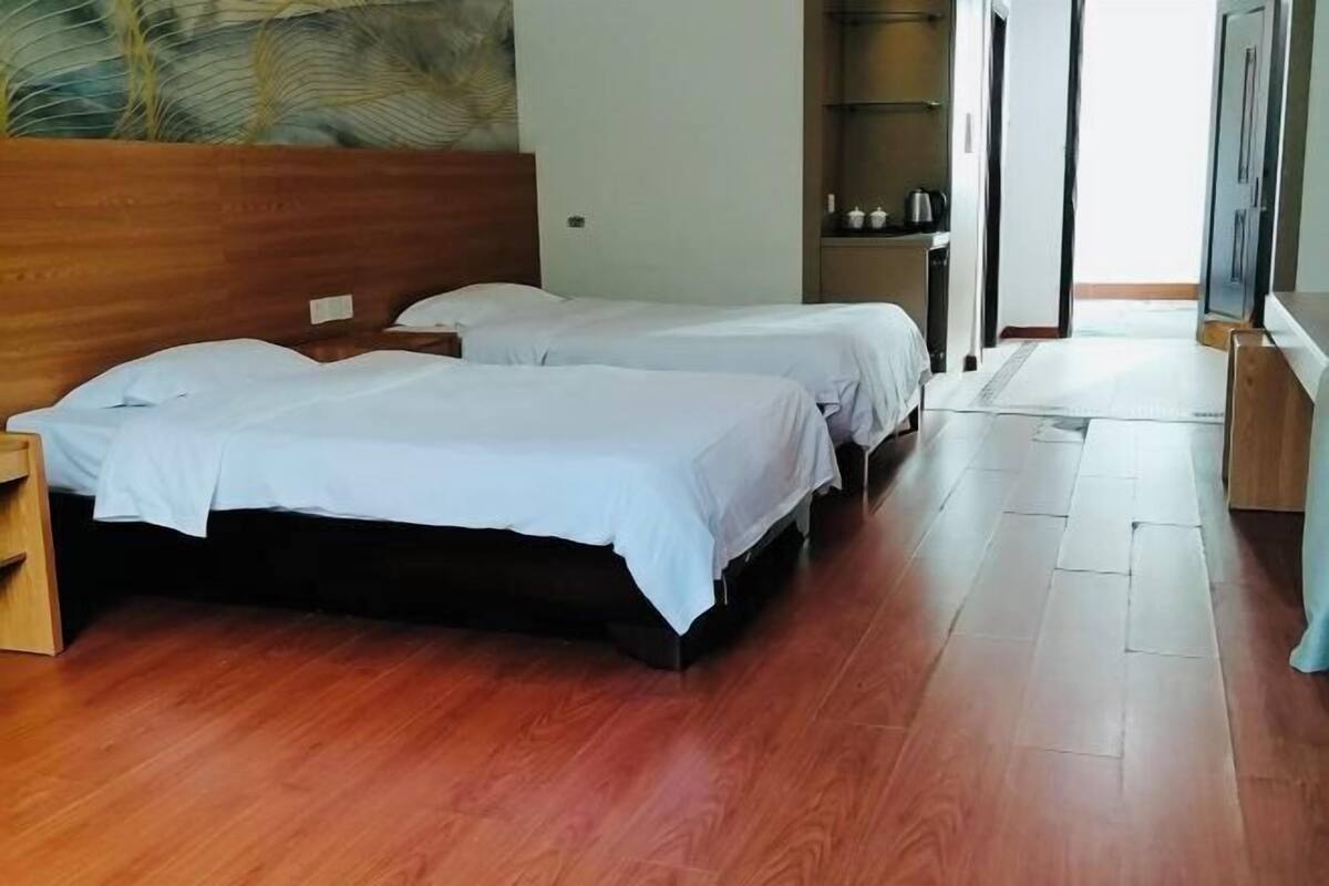 Een hotelkamer met twee bedden, houten vloeren, een nachtkastje, een wandplank en een deur naar een andere kamer.