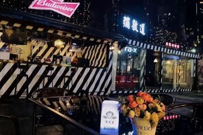 Un restaurant à la façade rayée, avec une enseigne Budweiser et une jardinière à l’extérieur.