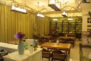A restaurant with tables and chairs, a counter with a vase, and hanging lights.