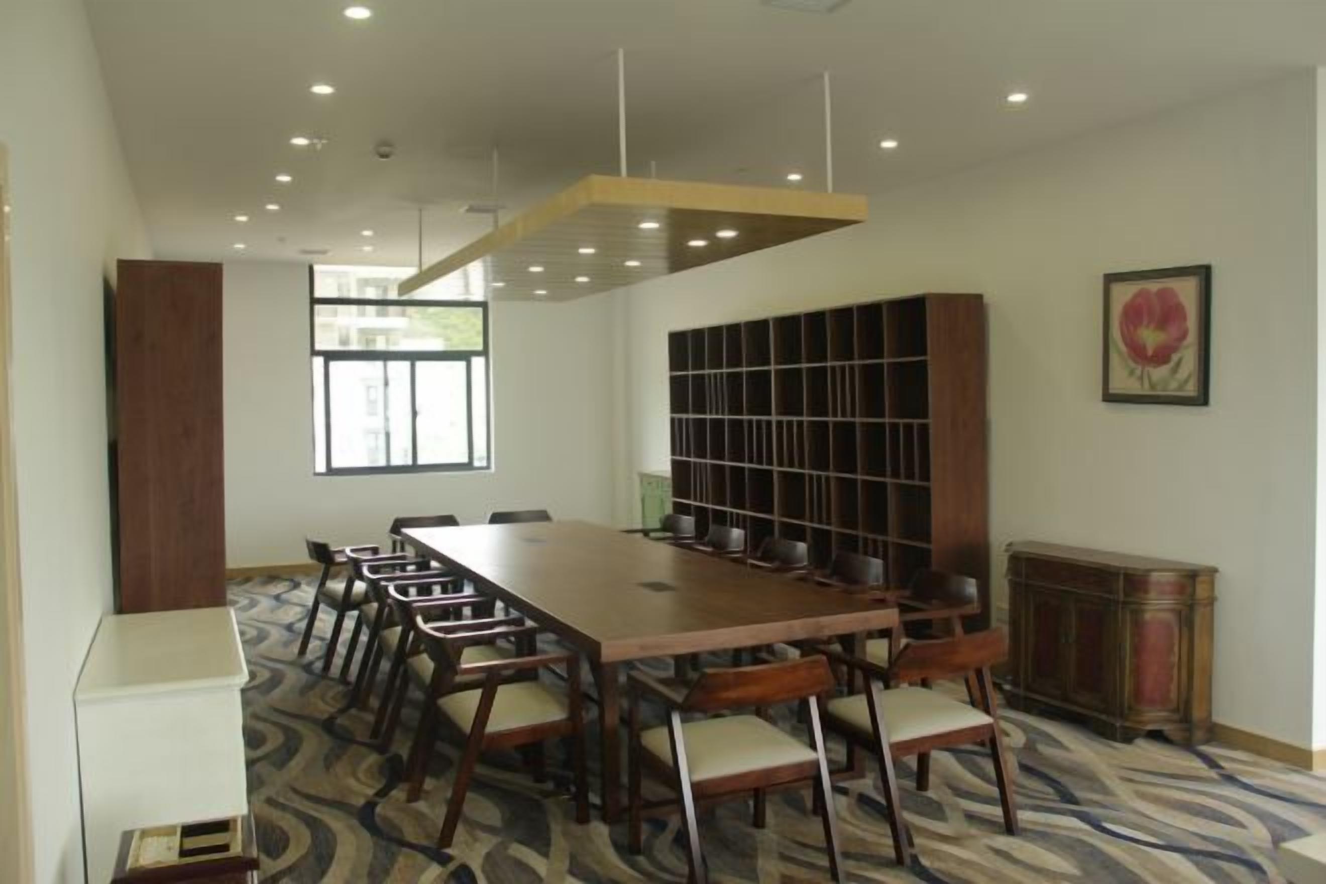 A conference room with a long table, chairs, a bookshelf, and a radiator.