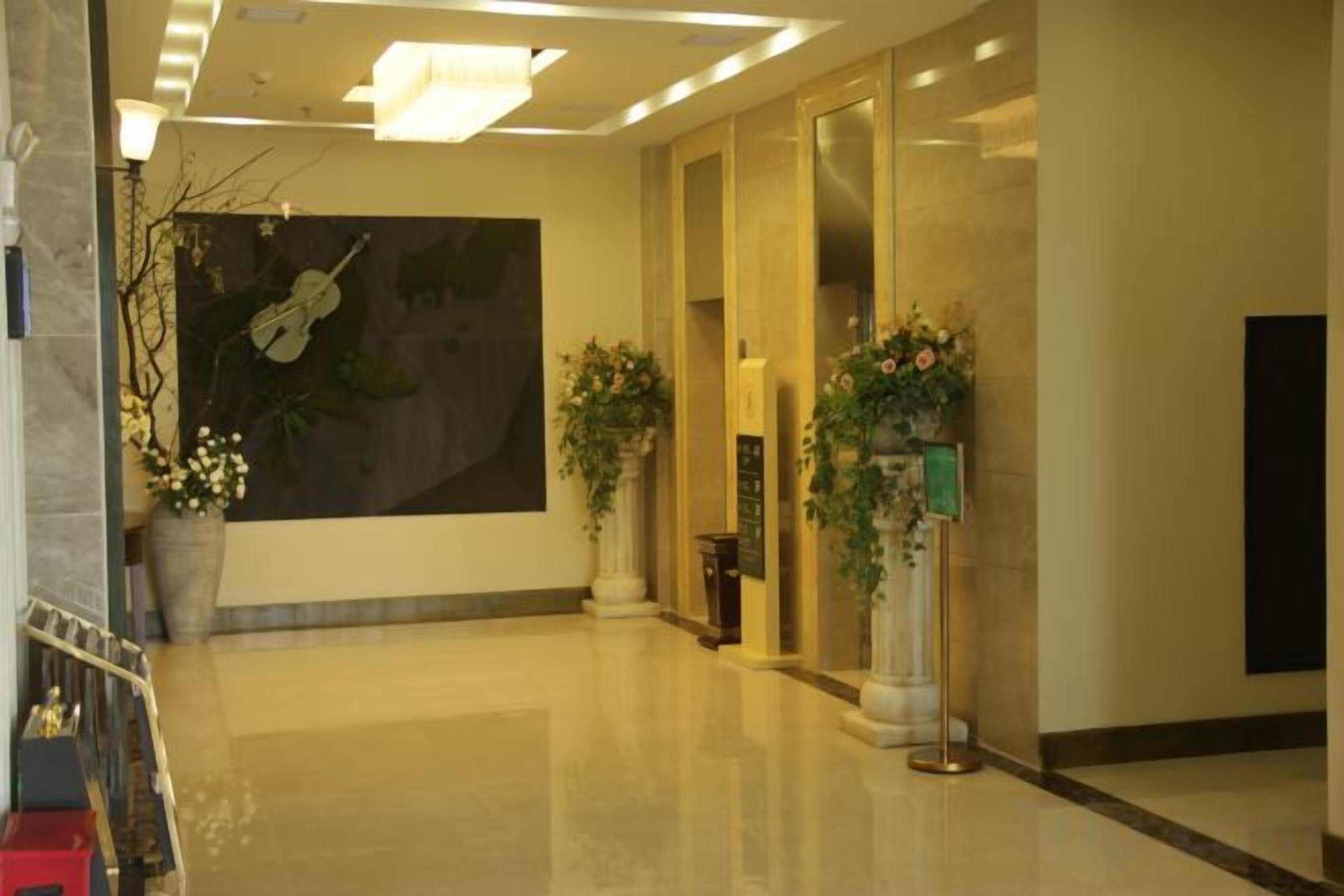A hotel lobby with a large wall mural, a reception desk, and potted plants.