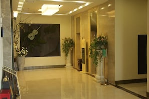 A hotel lobby with a large wall mural, a reception desk, and potted plants.