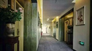 Un pasillo de hotel con suelo alfombrado, una planta en maceta a la izquierda y cuadros en las paredes.
