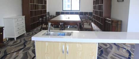 Un salón de conferencias con una mesa larga, sillas, una barra blanca con lavamanos y estanterías empotradas.