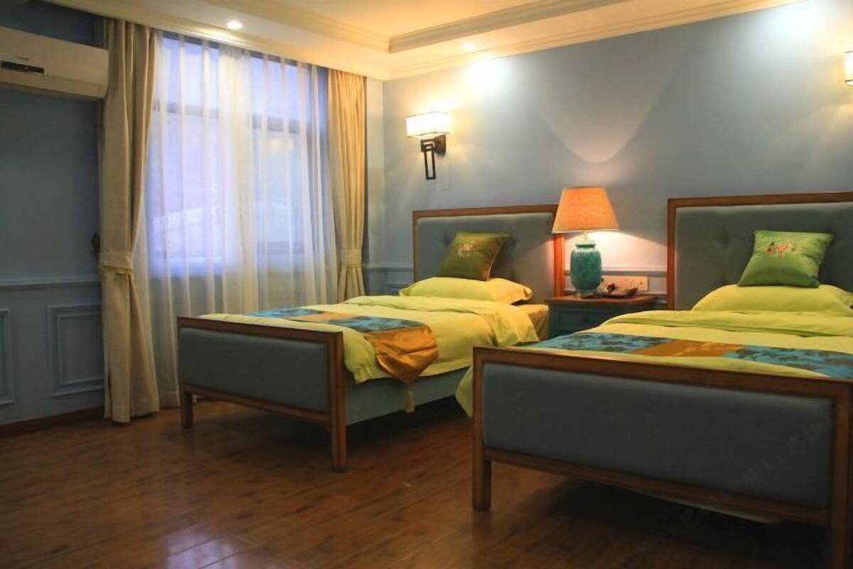 Une chambre d’hôtel avec deux lits simples, une table de chevet avec une lampe et une fenêtre avec des rideaux.