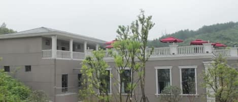 A building with a balcony, a covered walkway, and a view of a hilly landscape.