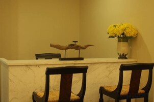 Una recepción con un jarrón de flores amarillas, dos sillas y un adorno en la pared.
