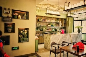 Interior de un restaurante con mostrador de mármol, estanterías con plantas y una zona de bar.