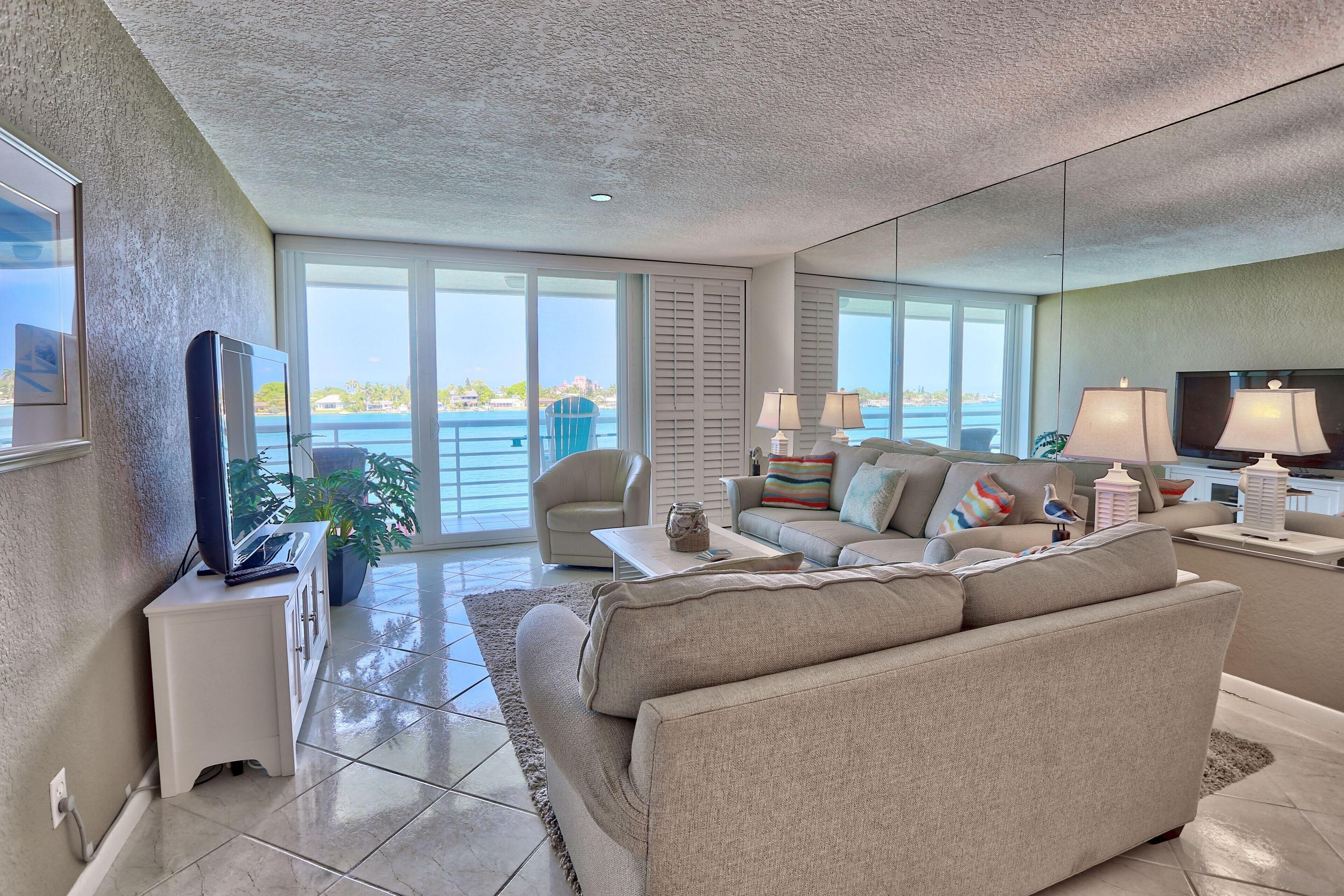 A spacious living room with a large sofa, a television, and a view of the ocean through large windows.