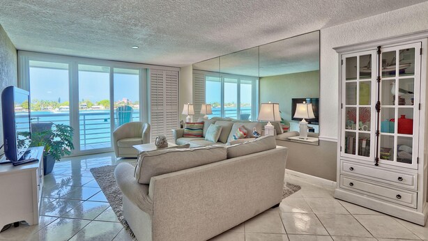 A spacious living room with a large window, a beige sofa, a white cabinet, and a television.