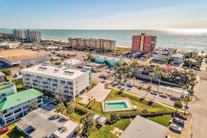 An aerial view of a coastal hotel area with multiple buildings, a parking lot, and a swimming pool. - Madeira Del Mar Penthouse #2- Premier (Madeira Beach)