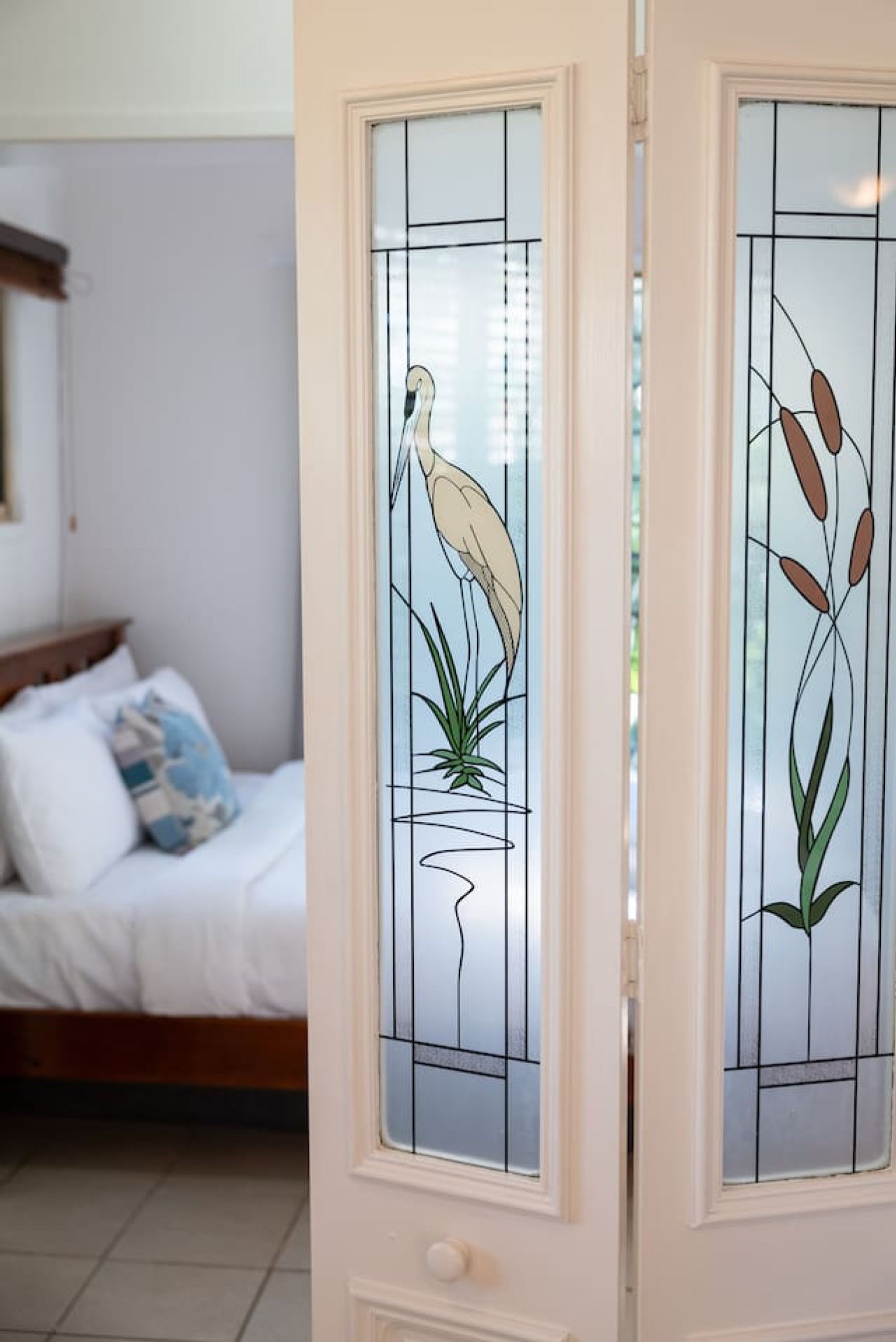 A room with a bed, a nightstand, and a window with a decorative glass panel featuring a bird and plant design.