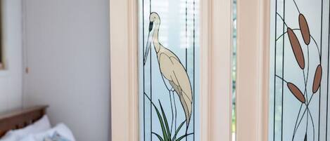 A room with a bed, a nightstand, and a window with a decorative glass panel featuring a bird and plant design.