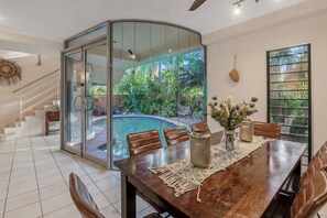 A dining area with a glass wall overlooking a swimming pool and lush greenery. - Zen Serene Seascape Family Pool BBQ Markets (Fannie Bay)