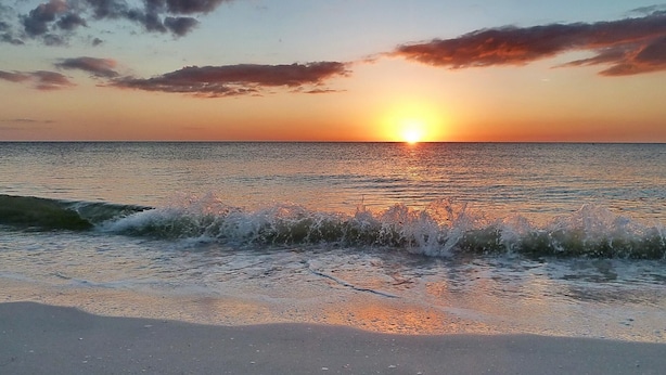 A sunset over a calm sea with waves gently touching the shore. - Good Vibrations - Beach House (Treasure Island)