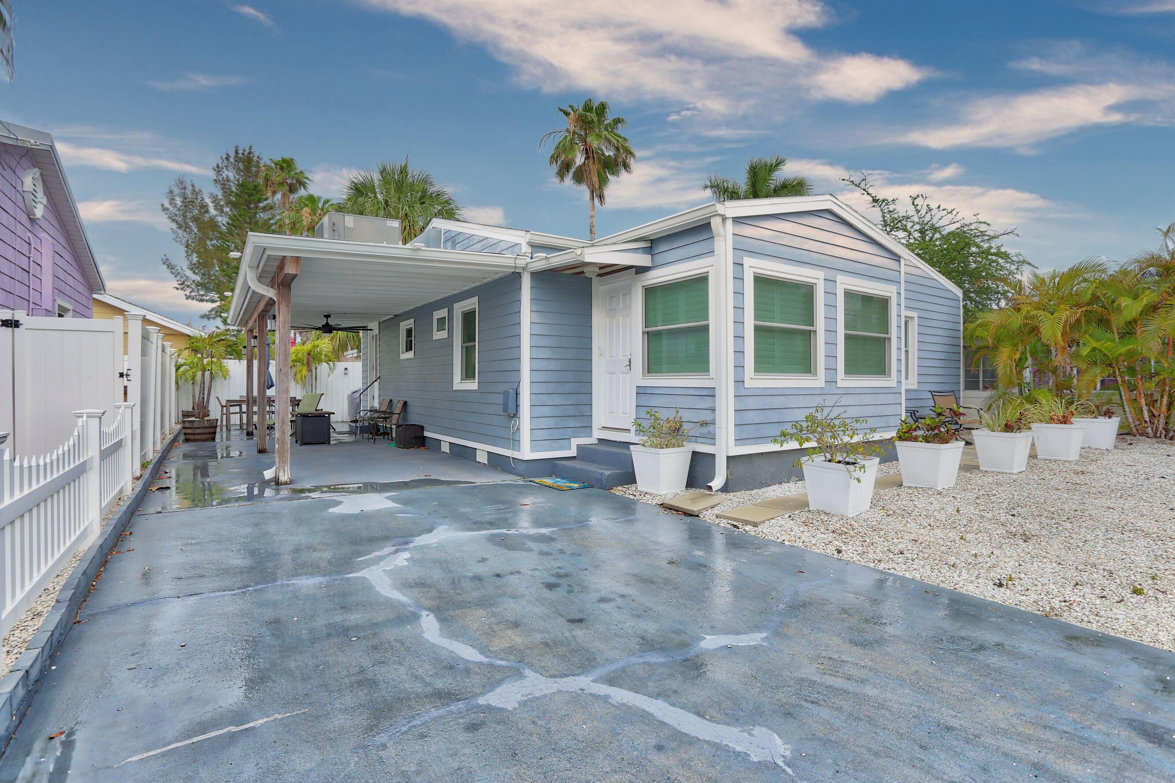 A single-story house with a covered porch, a concrete driveway, and potted plants.