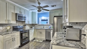 A kitchen with white cabinets, a stainless steel refrigerator, a microwave, a toaster, and a ceiling fan. - Good Vibrations - Beach House (Treasure Island)