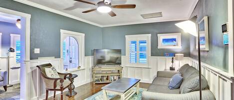 A living room with a ceiling fan, a television, a sofa, a coffee table, and a chair.