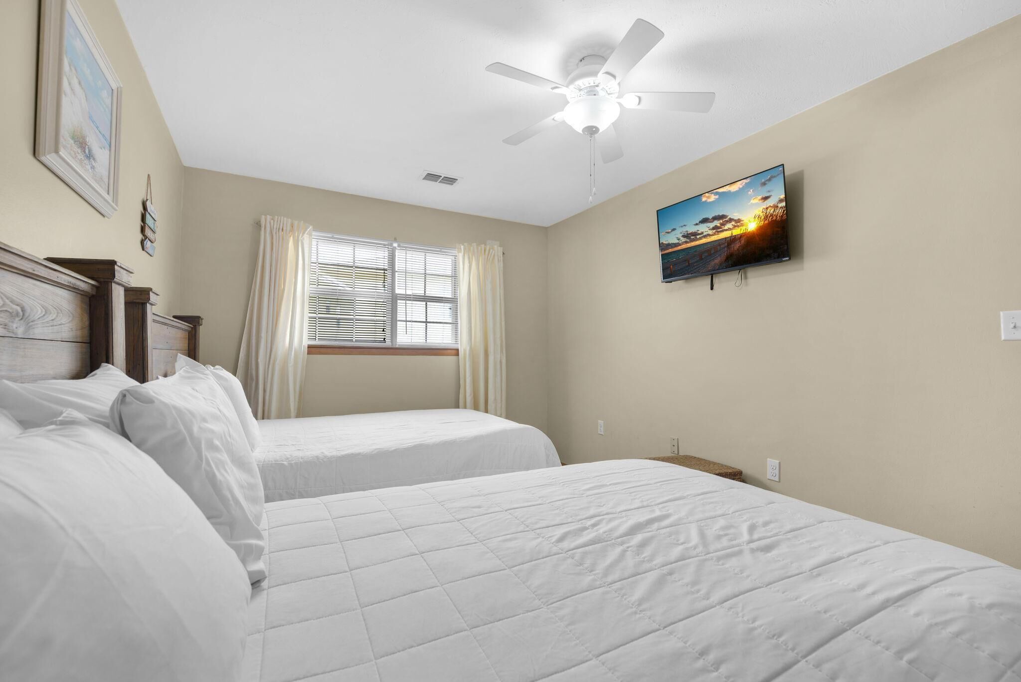 A bedroom with two beds, a ceiling fan, a window with curtains, and a painting on the wall.