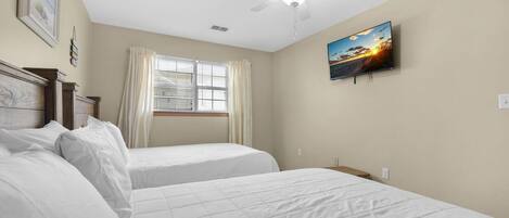 A bedroom with two beds, a ceiling fan, a window with curtains, and a painting on the wall.