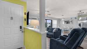 A modern living room with a sofa, a dining area with a table and chairs, and a kitchen with a refrigerator. - Sugar Dunes 211 (Navarre)