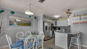 A kitchen with white cabinets, a stainless steel refrigerator, a dining table with chairs, and a small island with stools. - Sugar Dunes 211 (Navarre)