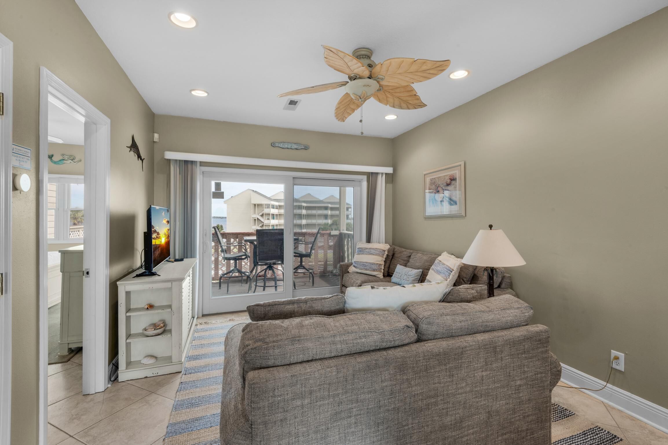 A living room with a ceiling fan, a sofa, a TV, and a view of the outside balcony.