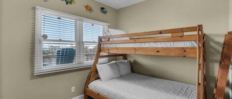 A bunk bed with a wooden frame and white bedding, a ceiling fan, and a window with blinds.