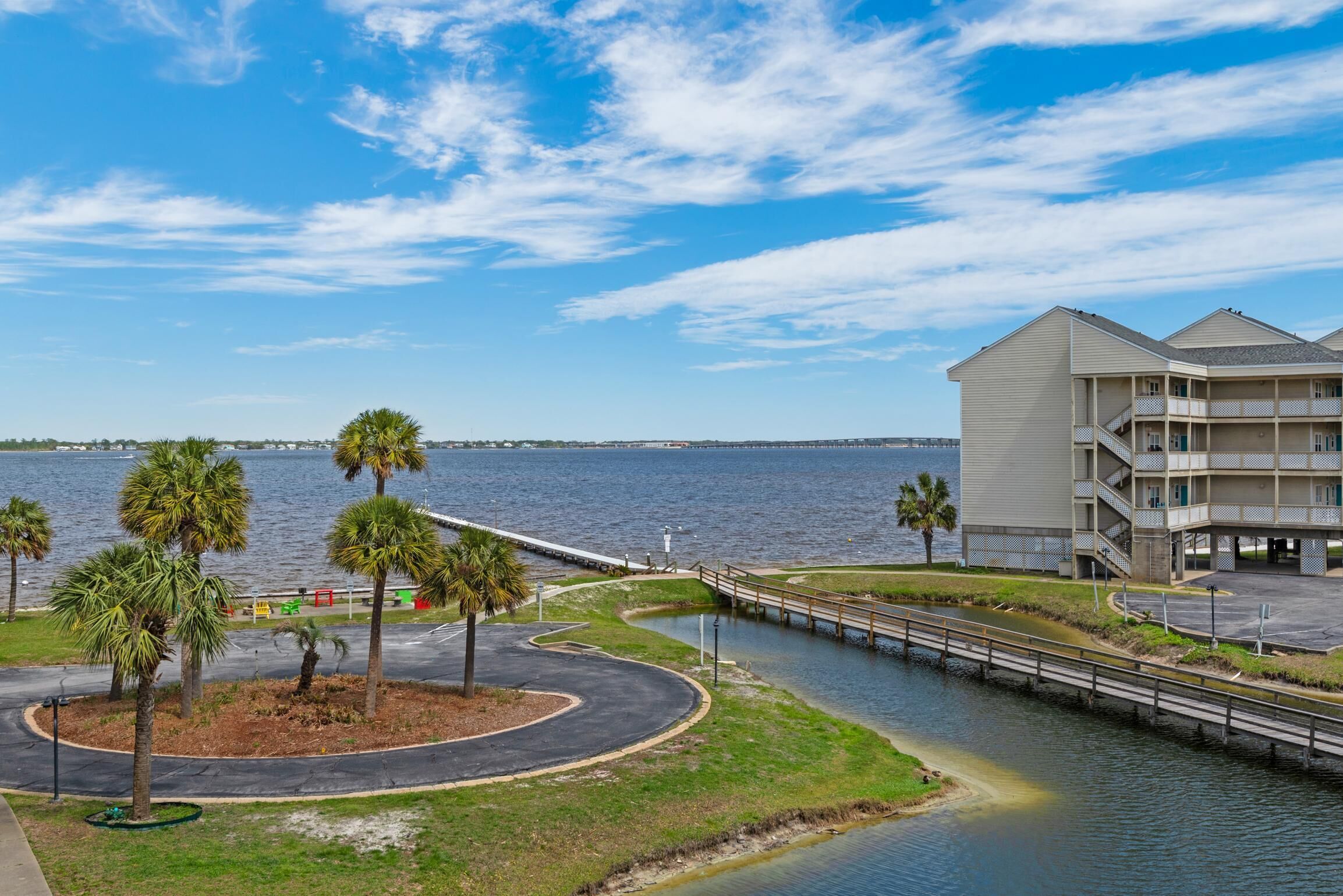 A waterfront property with a curved road, palm trees, and a building with balconies.