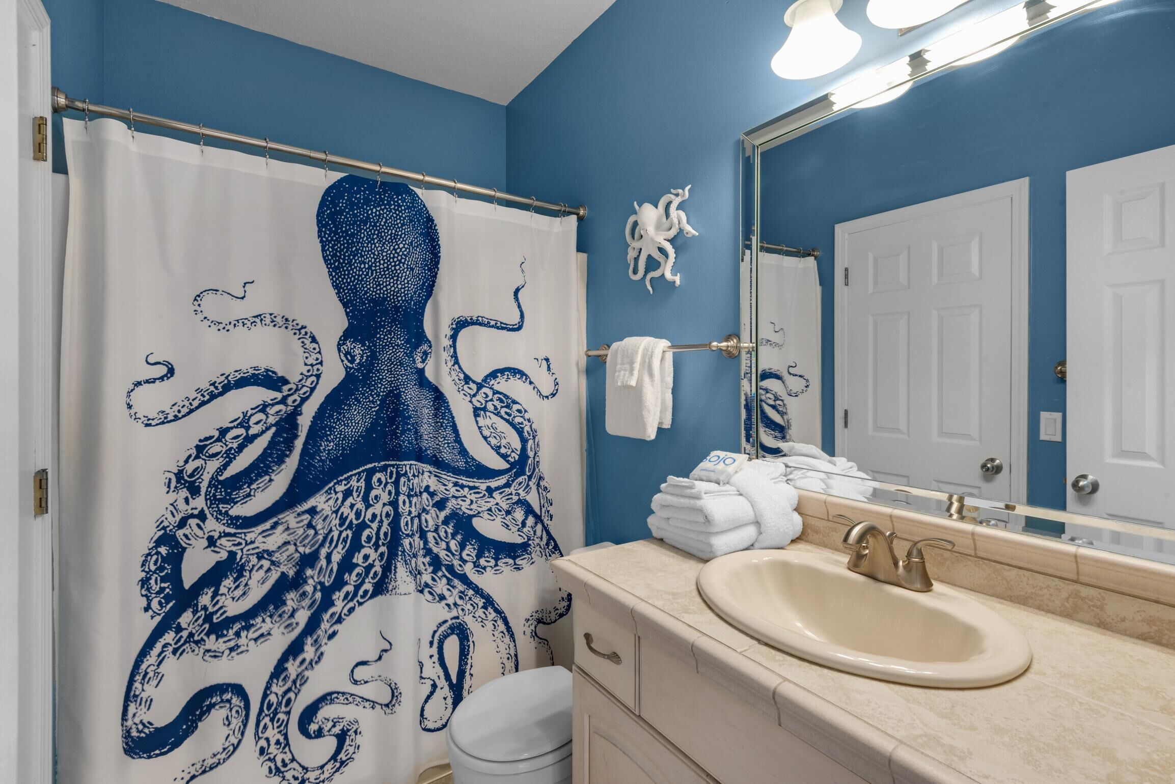 A bathroom with a blue octopus shower curtain, a sink, and a mirror.