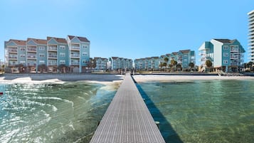 Hotel frente al mar con un muelle largo que llega a la playa, con varios balcones y una vista despejada del océano.