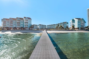 Hotel frente al mar con un muelle largo que llega a la playa, con varios balcones y una vista despejada del océano.