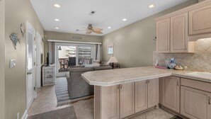 A kitchen with beige cabinets, a countertop, and a ceiling fan. - Baywatch C8 (Pensacola Beach)