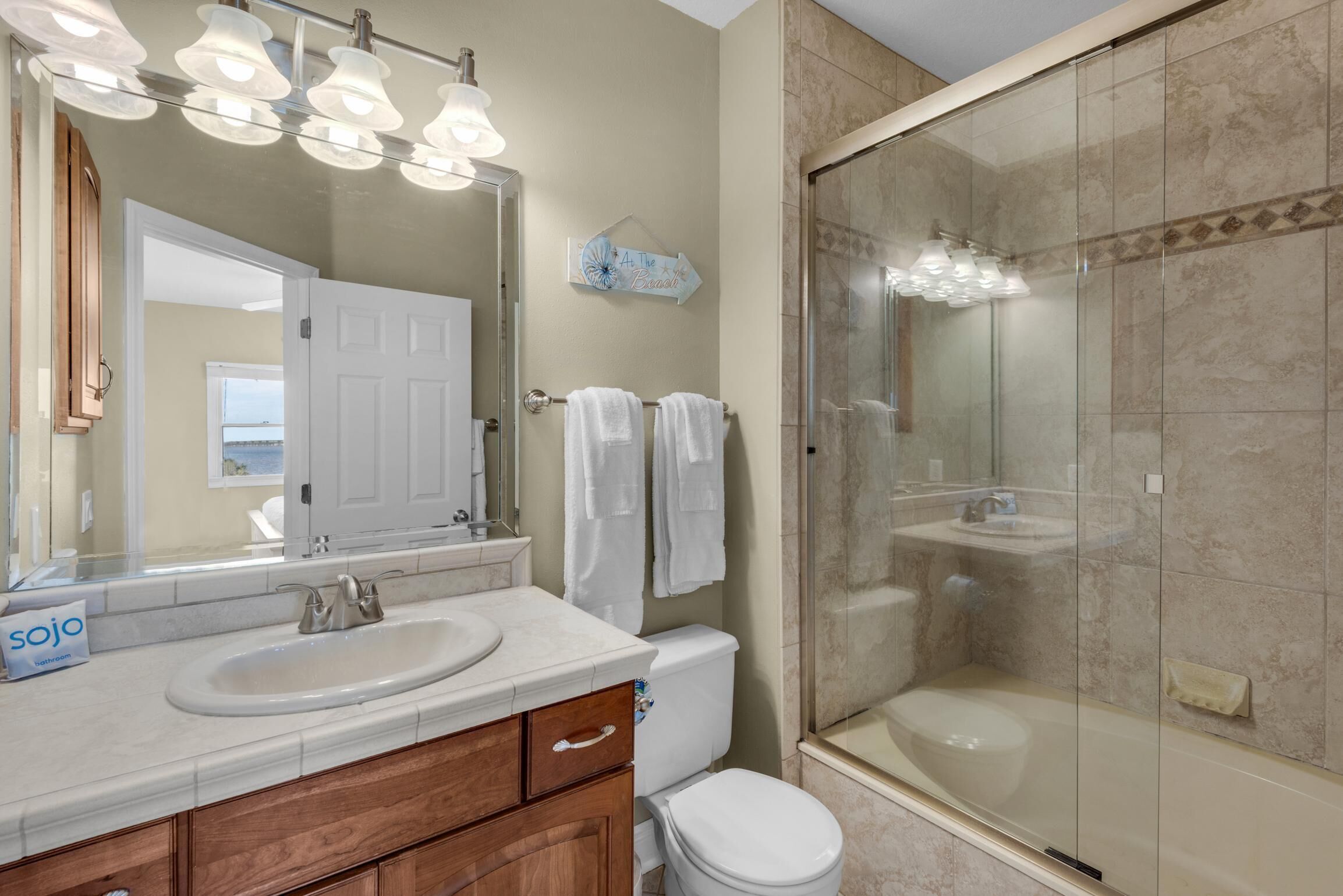 Une salle de bain moderne avec un grand miroir, un lavabo, des toilettes et une douche à parois de verre.