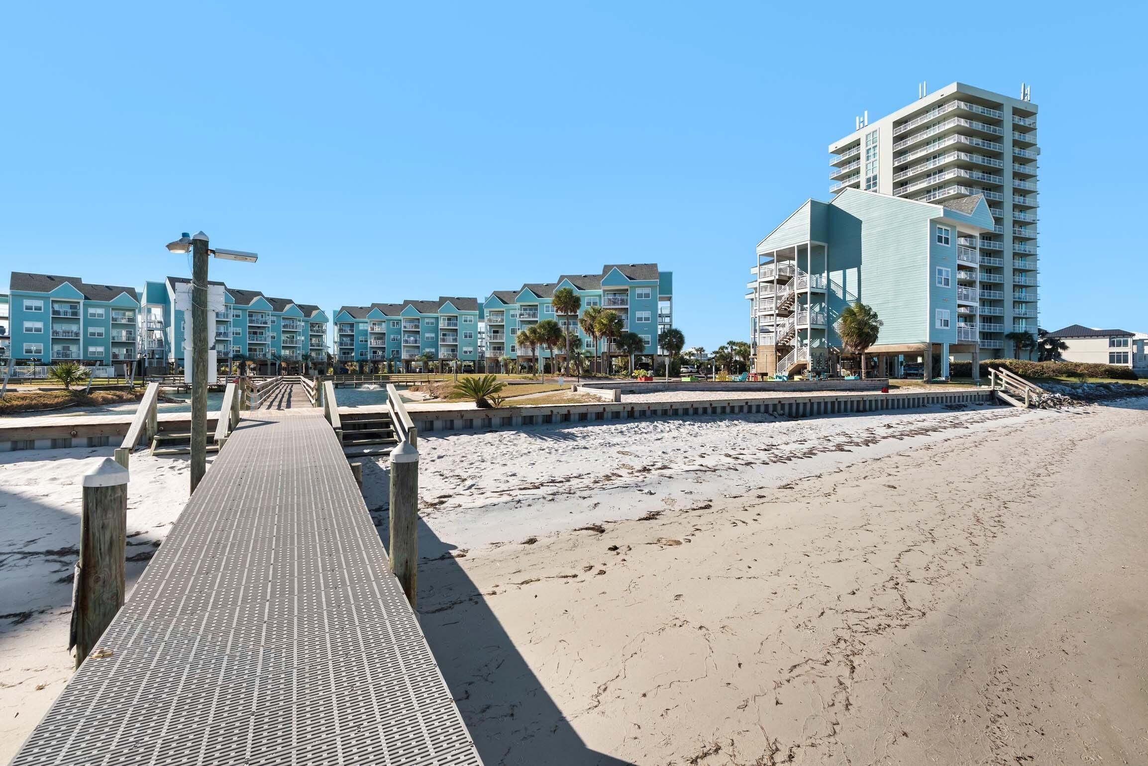 A beachside hotel with a boardwalk leading to the beach, featuring multiple-story buildings with balconies.
