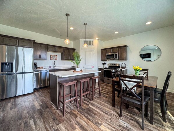A modern kitchen with stainless steel appliances, a central island with bar stools, wooden flooring, and pendant lighting. - Avani Home, Dog friendly, close to Market/Marina (Garden City)