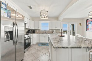 A modern kitchen with stainless steel appliances, white cabinetry, a marble countertop, and a pendant light. - Sea Forever (Pensacola Beach)