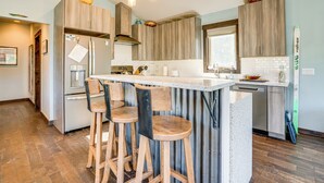 A modern kitchen with wooden cabinets, a central island with bar stools, stainless steel appliances, and a large window providing natural light. - Hike, Soak & Play: Keystone Home w/ Views! (Keystone)