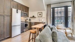 Une cuisine moderne avec des meubles en bois, des appareils électroménagers en acier inoxydable et un coin repas comprenant une table en bois et des tabourets de bar.