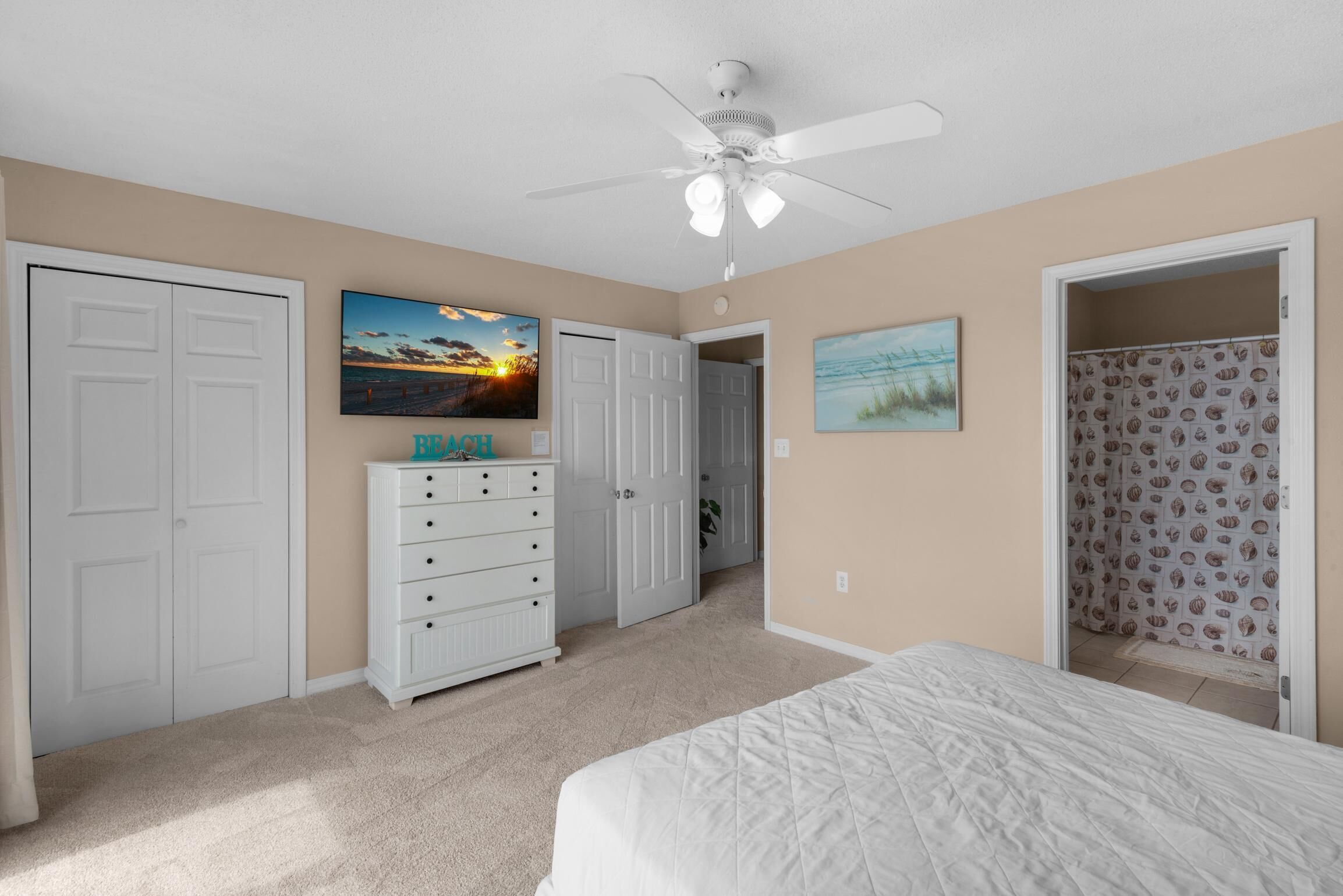 A bedroom with a bed, a dresser, a ceiling fan, and two doors.