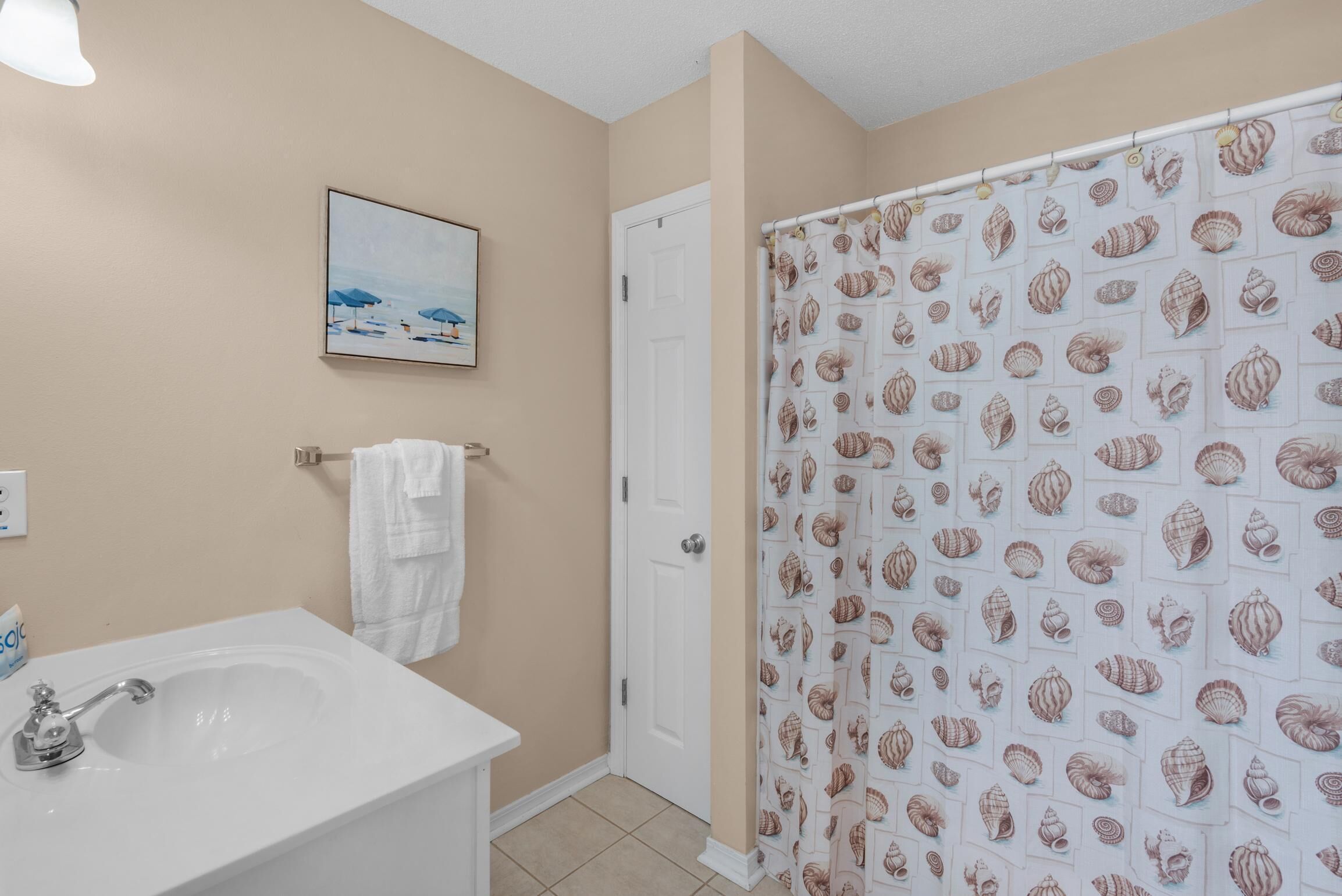 A bathroom with a bathtub, a sink, a towel rack, and a shower curtain with a shell pattern.