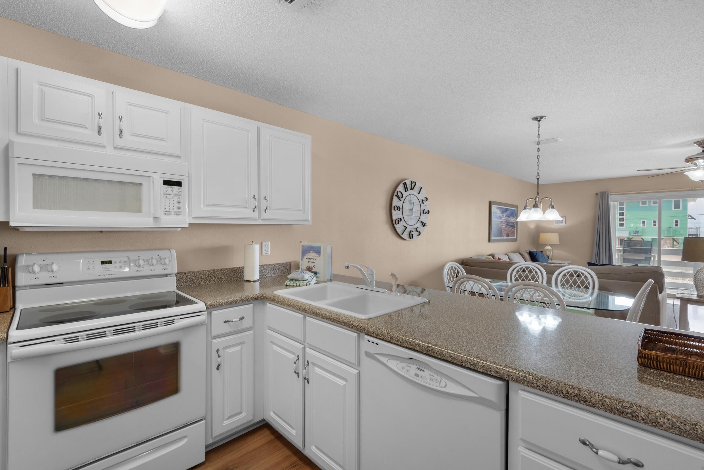 A kitchen with white cabinets, a microwave, an oven, a sink, and a dining area with a table and chairs.