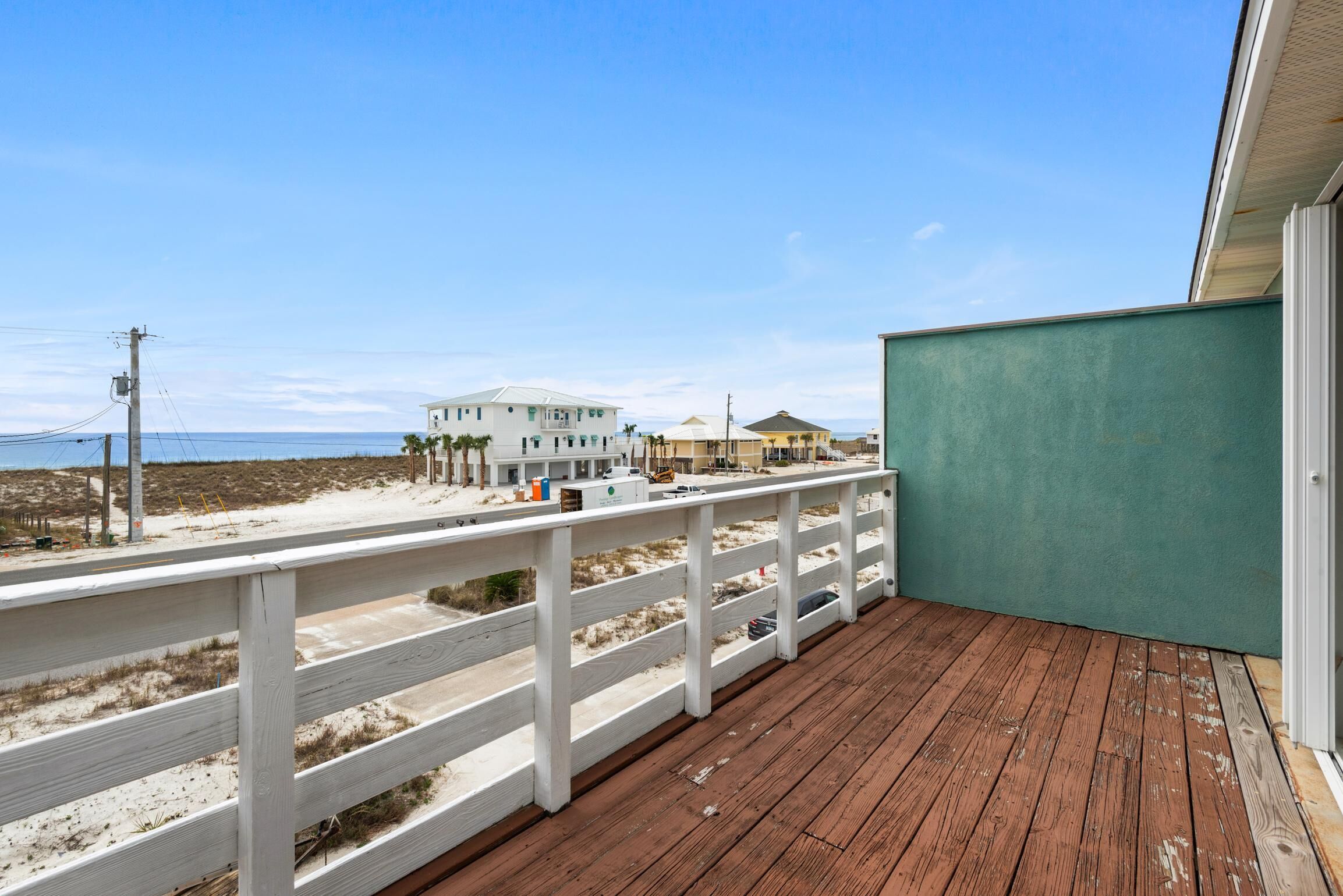 A wooden deck with a white railing overlooking a beach with buildings in the distance.