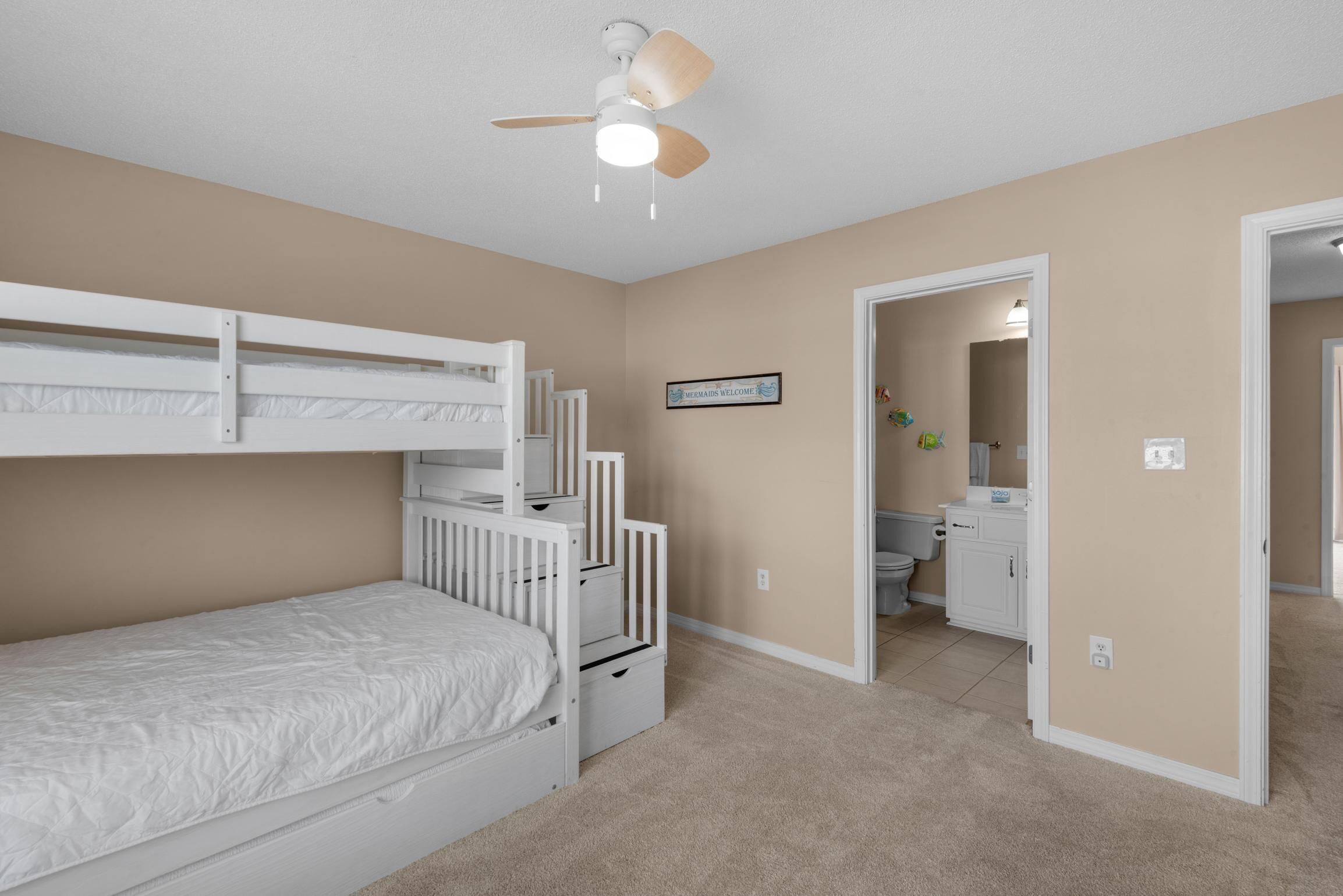 A bedroom with bunk beds, a ceiling fan, a bathroom with a toilet and sink, and a welcome sign.