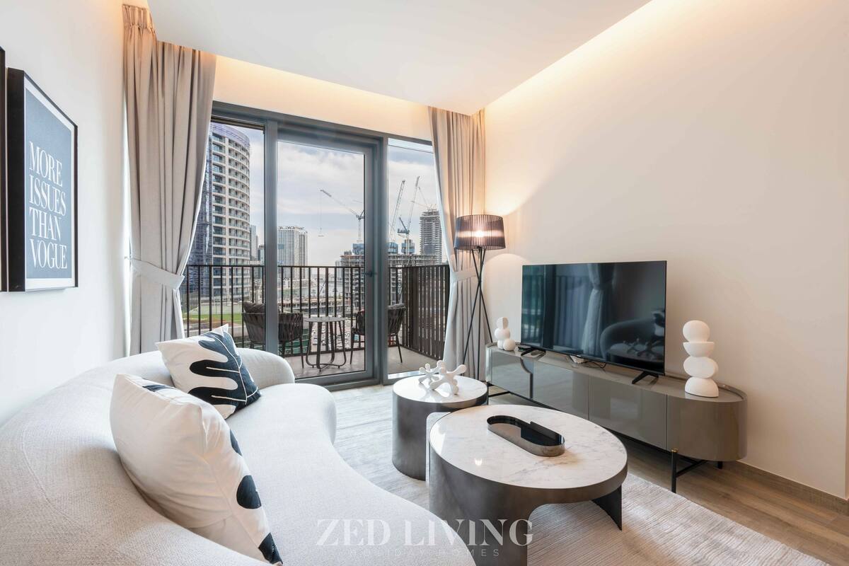 A modern living room with a sofa, a coffee table, a TV, and a balcony with a view of the cityscape.