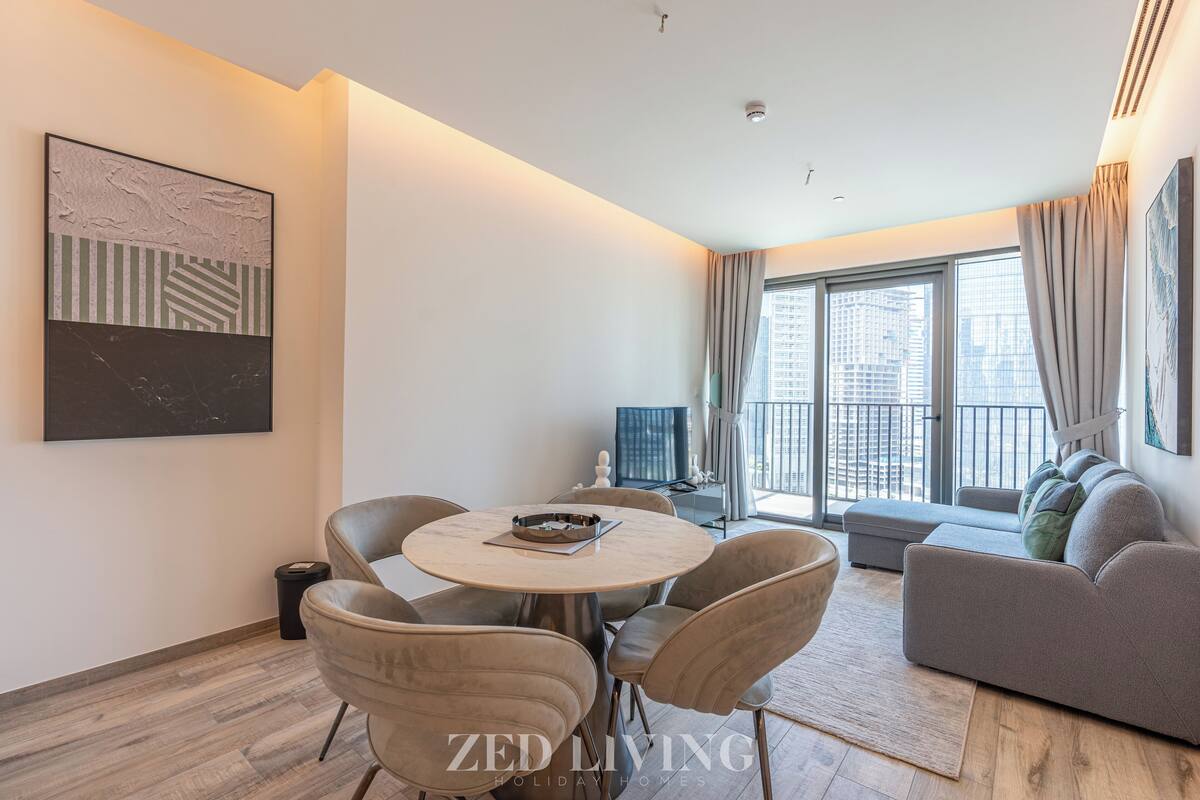A modern living room with a round table, comfortable seating, a sofa, and large windows offering a city view.